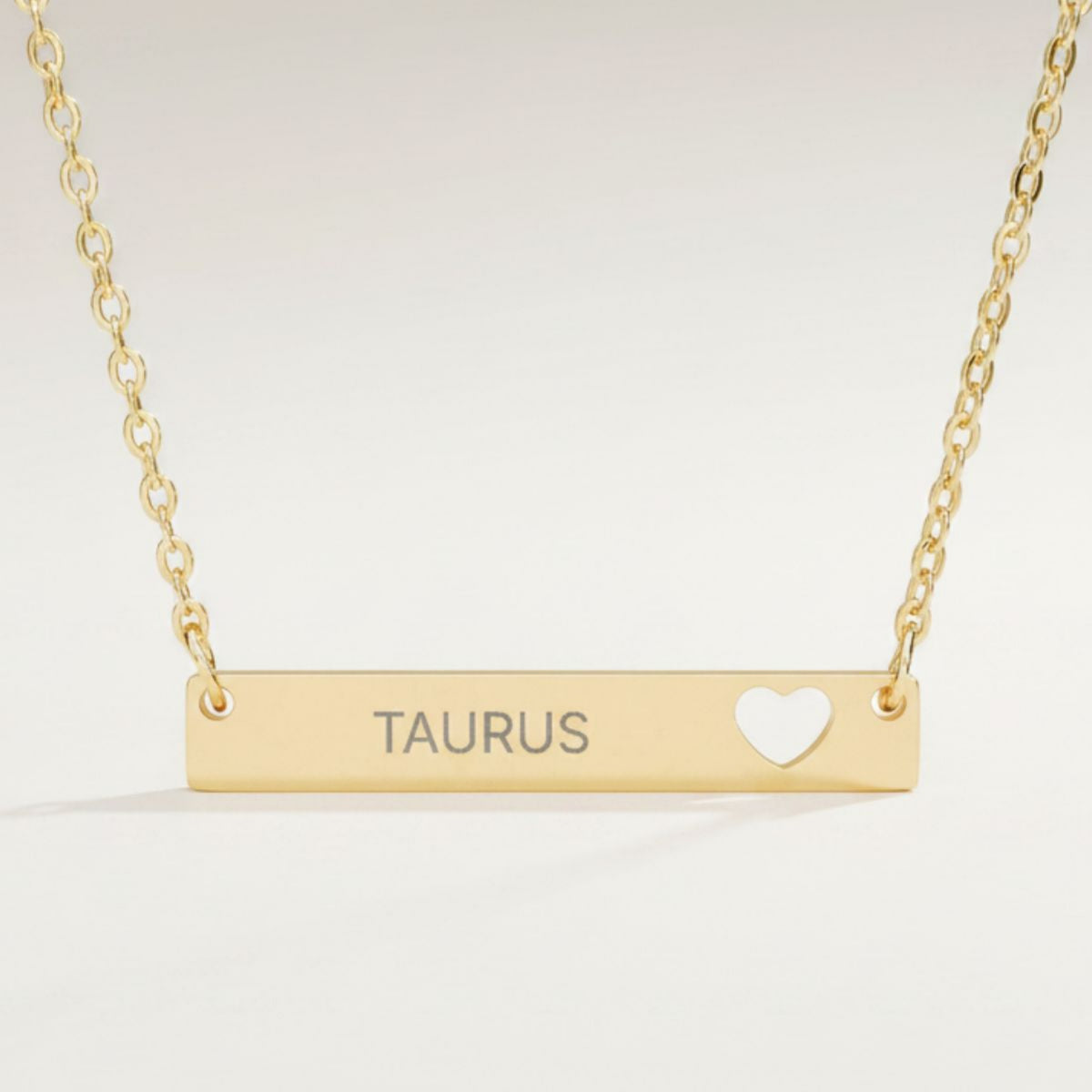Taurus zodiac necklace close-up — 18K Gold polished cutout heart bar pendant with grey laser-etched TAURUS, see-through heart cutout, premium macro on white background