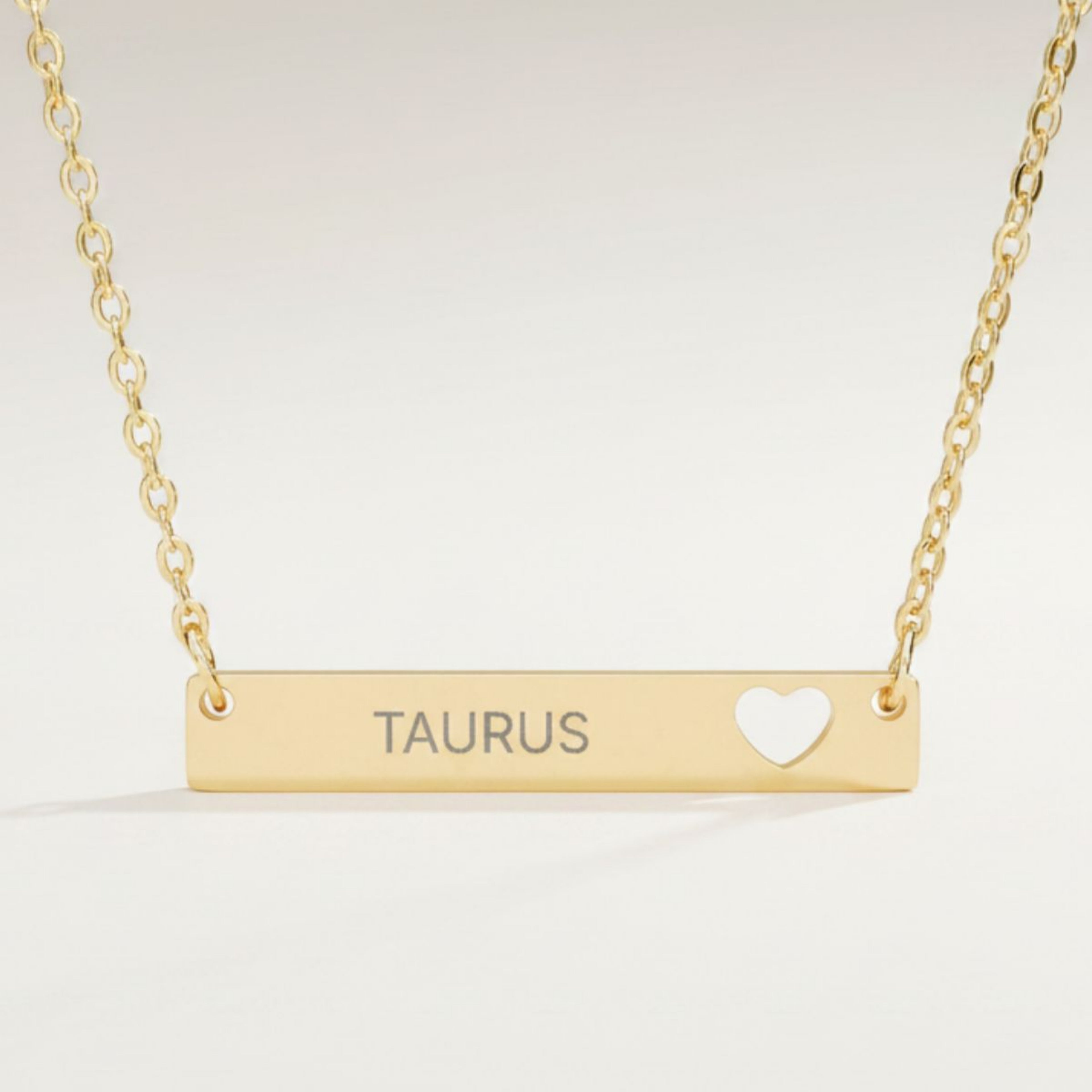 Taurus zodiac necklace close-up — 18K Gold polished cutout heart bar pendant with grey laser-etched TAURUS, see-through heart cutout, premium macro on white background