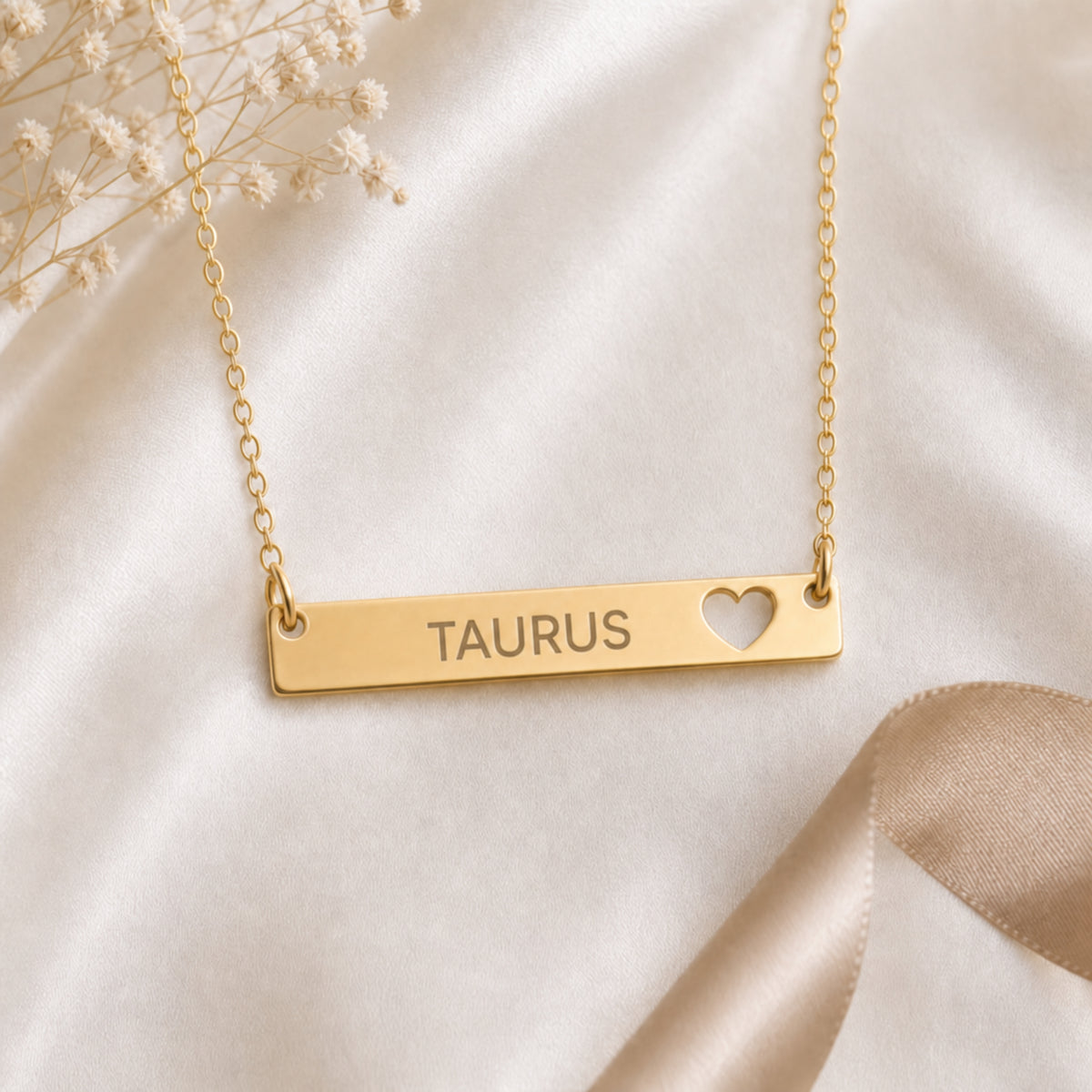 Cream-linen flat lay of the Taurus zodiac necklace — 18K Gold cutout heart bar pendant with grey laser-etched TAURUS, dried baby's breath, editorial styling