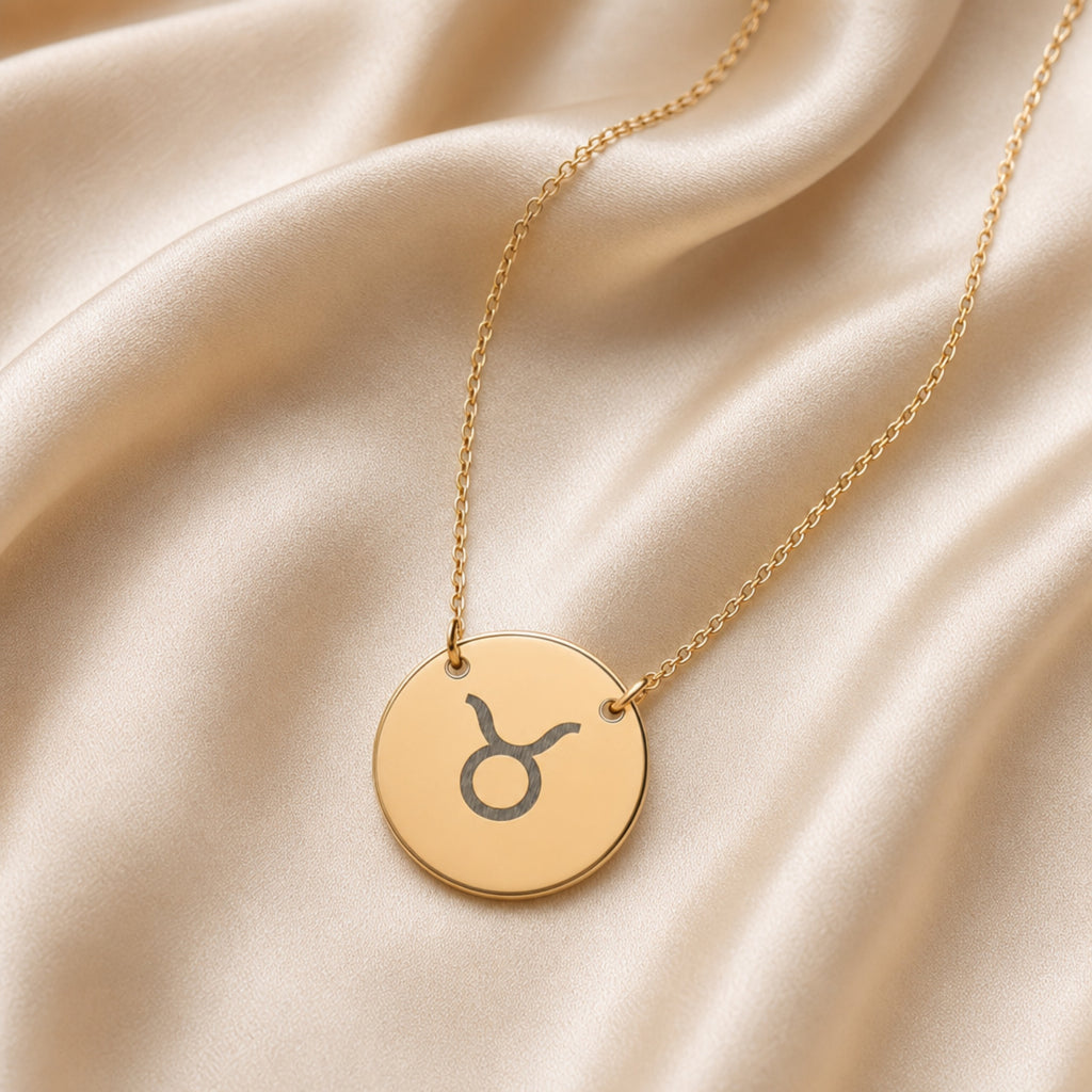 Taurus zodiac coin necklace flatlay — 18K gold pendant with laser-engraved Taurus Bull glyph on cream linen
