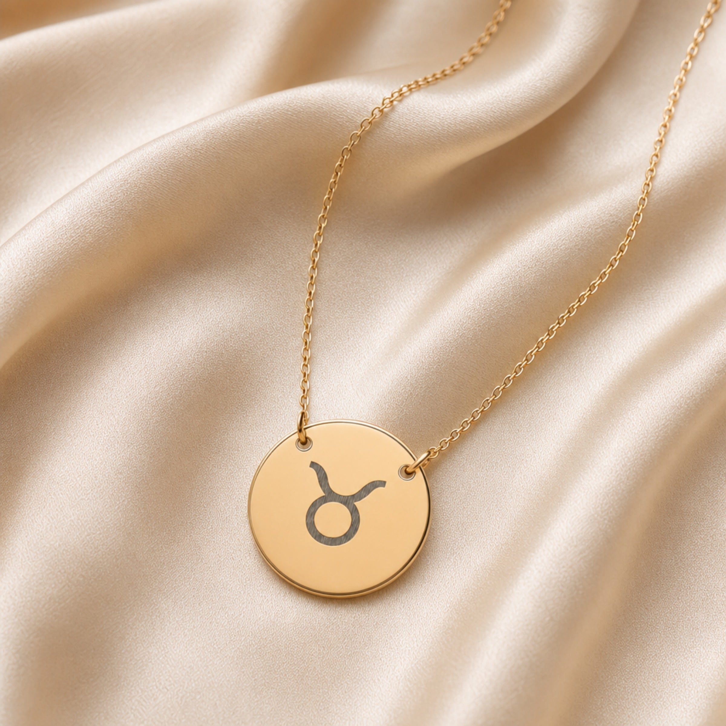 Taurus zodiac coin necklace flatlay — 18K gold pendant with laser-engraved Taurus Bull glyph on cream linen