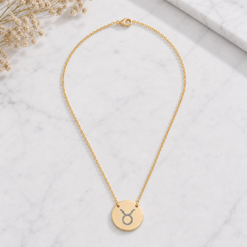 Taurus zodiac coin necklace marble flatlay — 18K gold pendant engraved with Taurus Bull star sign on white marble with dried floral, premium personalized astrology necklace gift for May birthday, Taurusian present