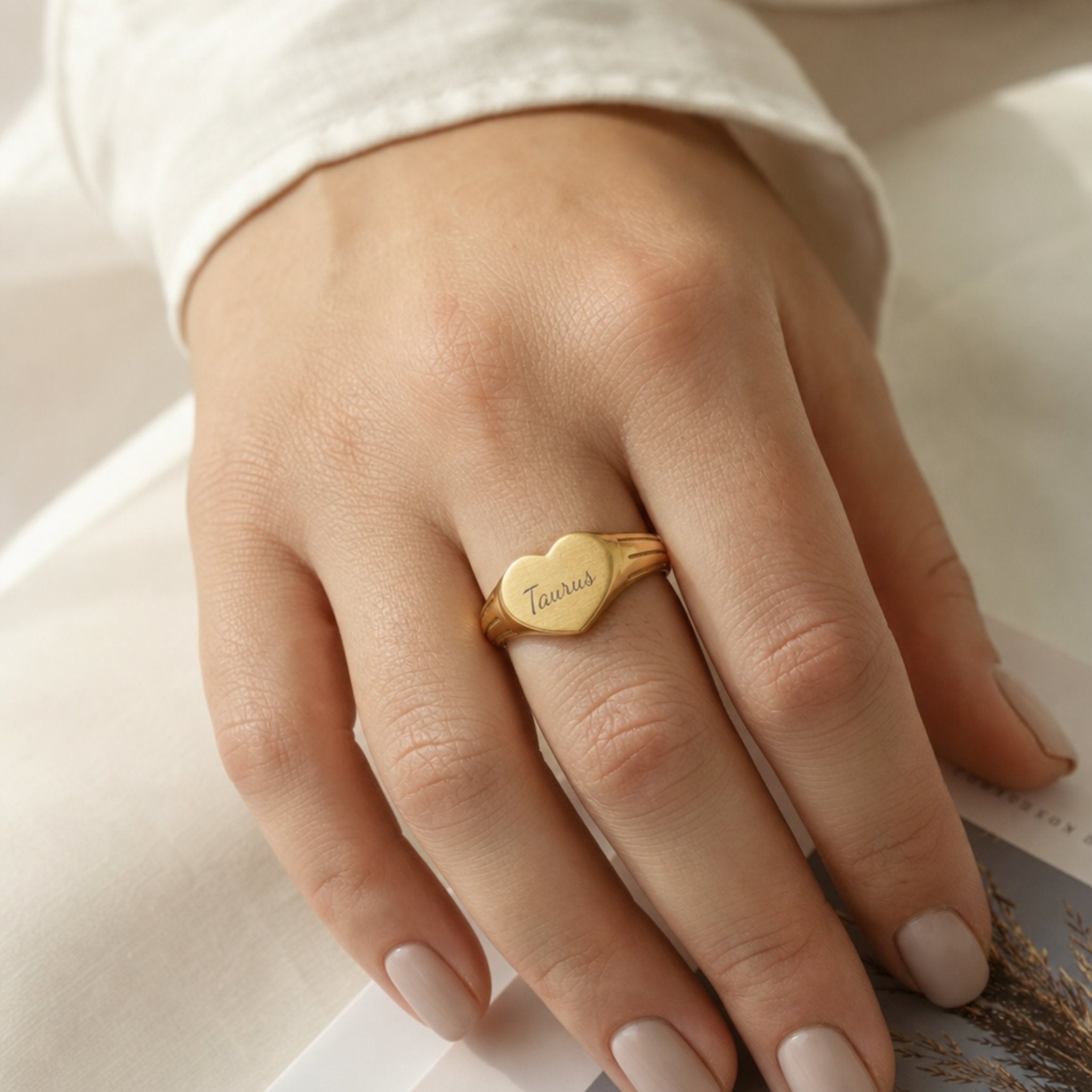 Taurus zodiac heart signet ring on finger — model wearing engraved Taurus heart signet, cream linen lifestyle moment