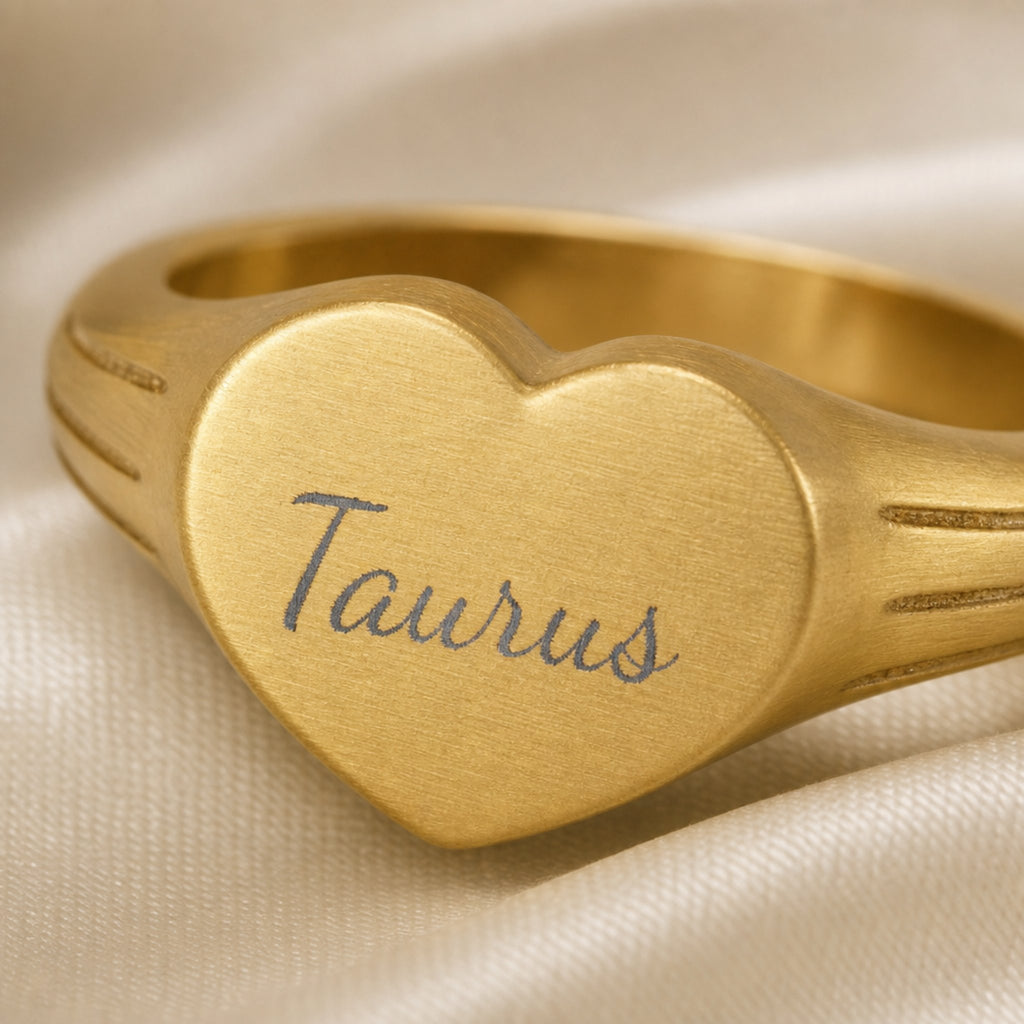 Taurus zodiac heart signet ring engraving close-up — laser-etched Taurus name detail, brushed grey cursive on matte gold heart