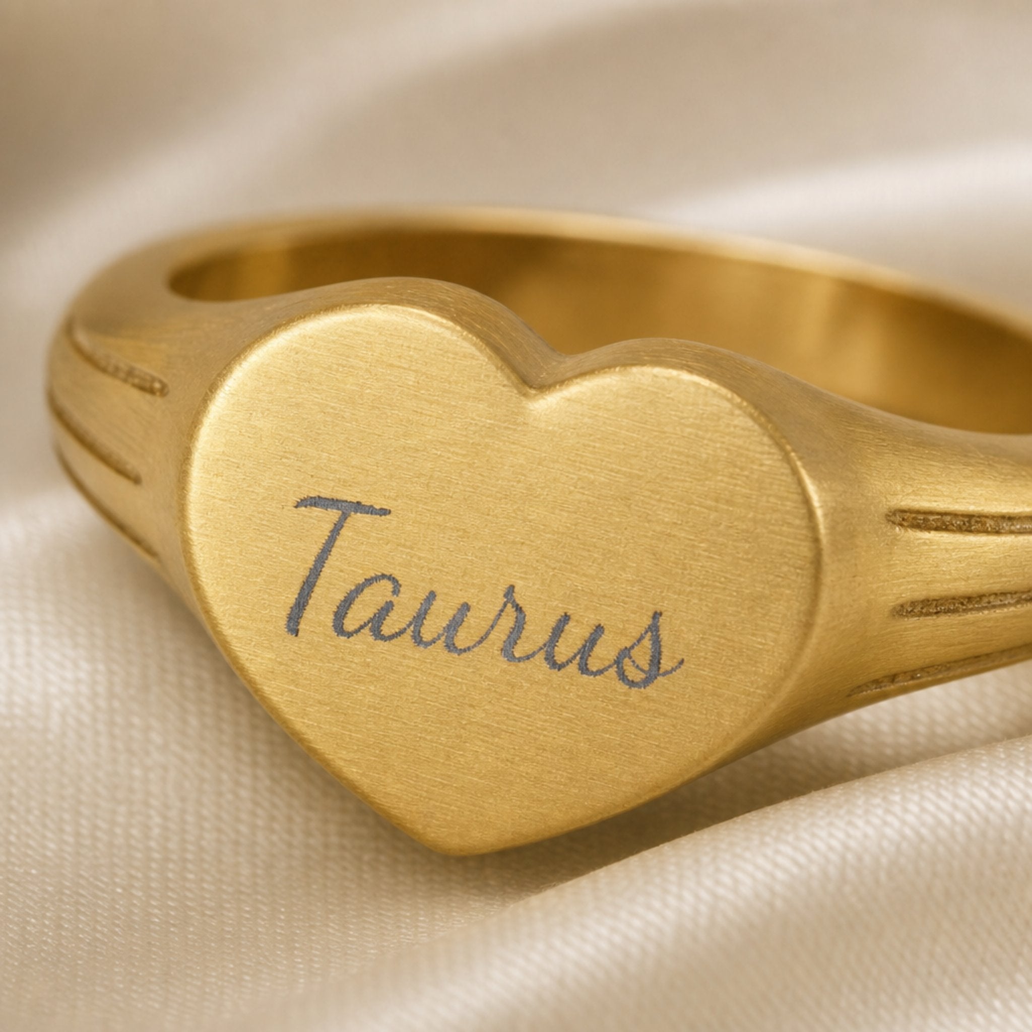 Taurus zodiac heart signet ring engraving close-up — laser-etched Taurus name detail, brushed grey cursive on matte gold heart