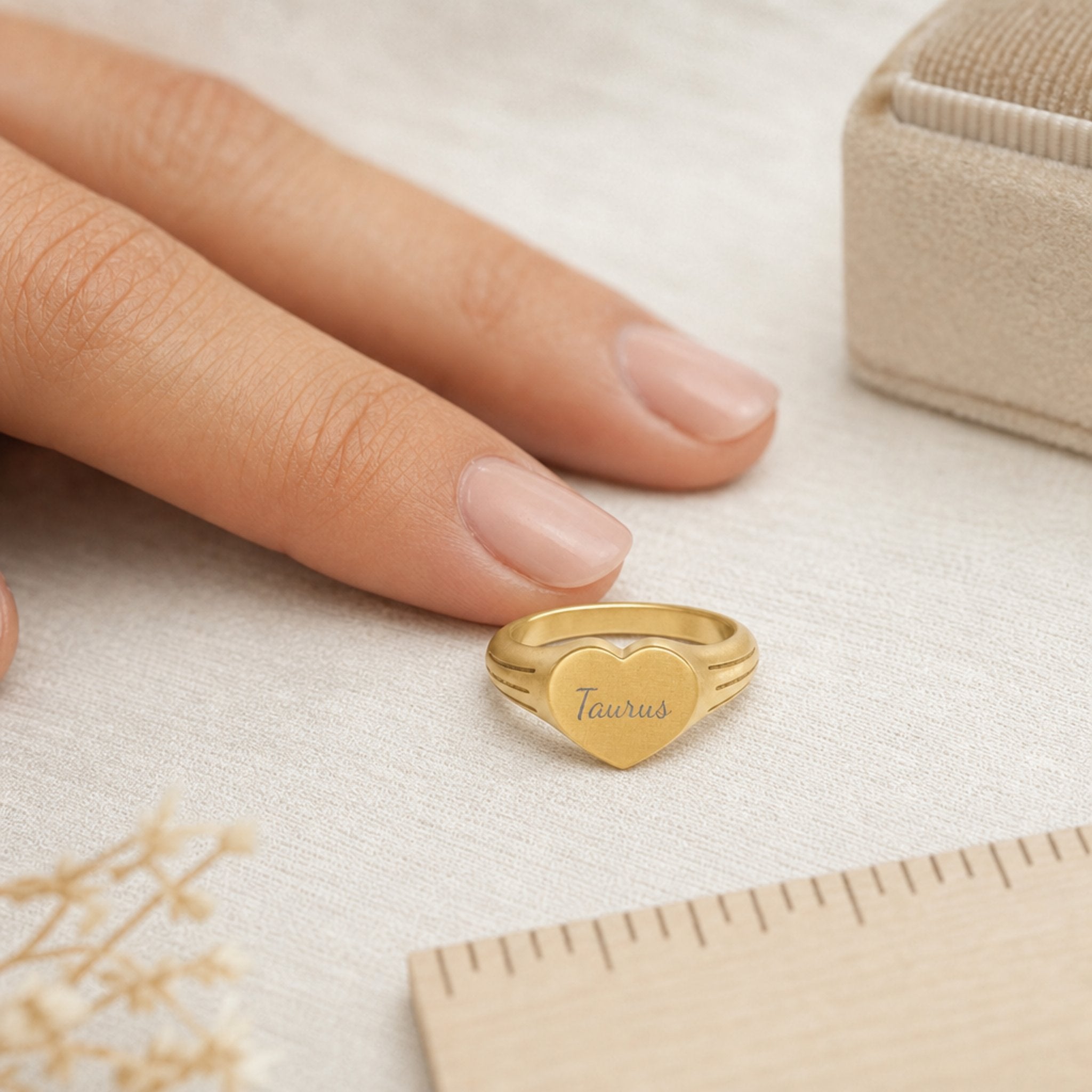 Taurus zodiac heart signet ring scale-in-hand — fingers holding heart ring next to gift box and ruler, dainty signet sizing