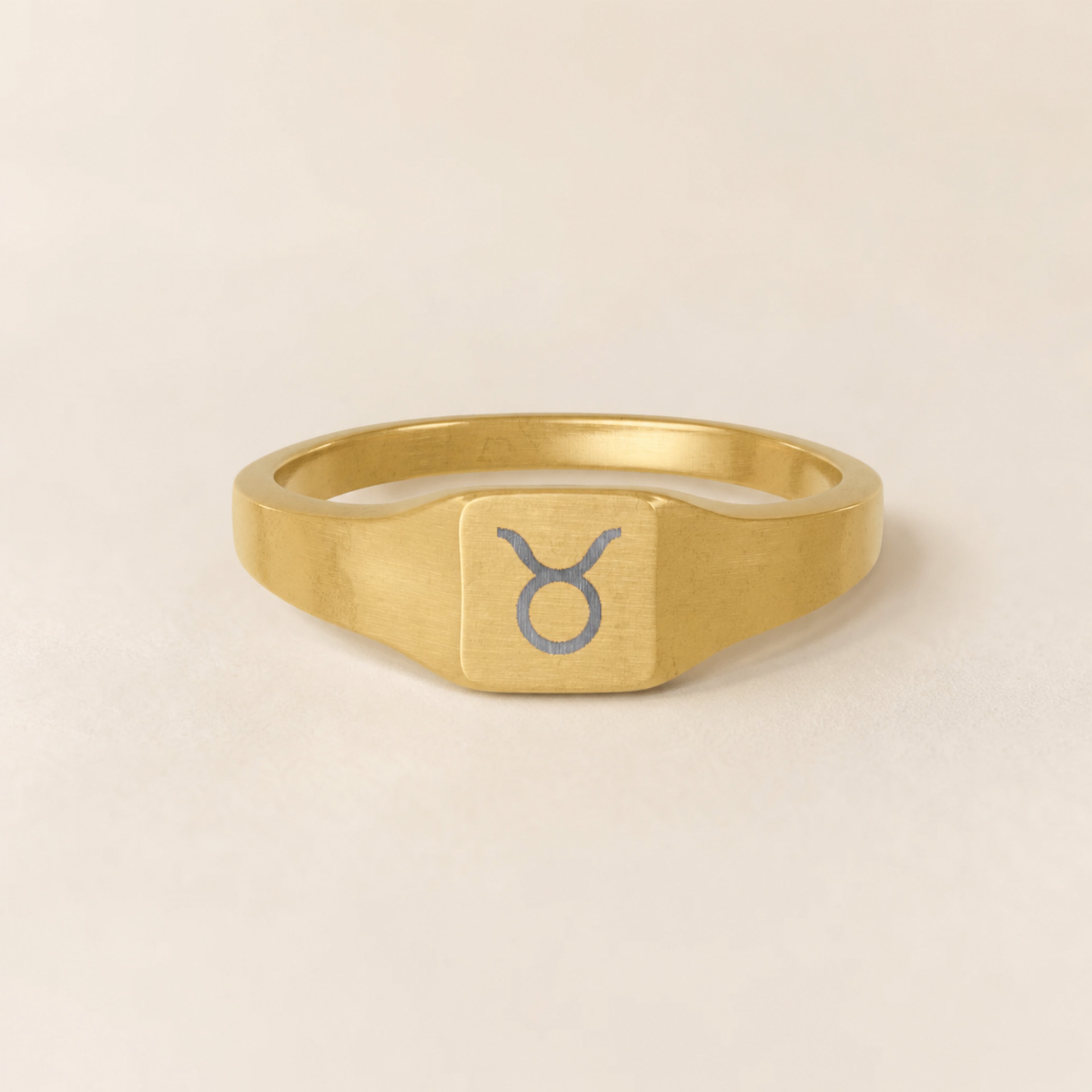 Taurus zodiac square signet ring studio front — clean cream backdrop product shot, 18K gold matte PVD
