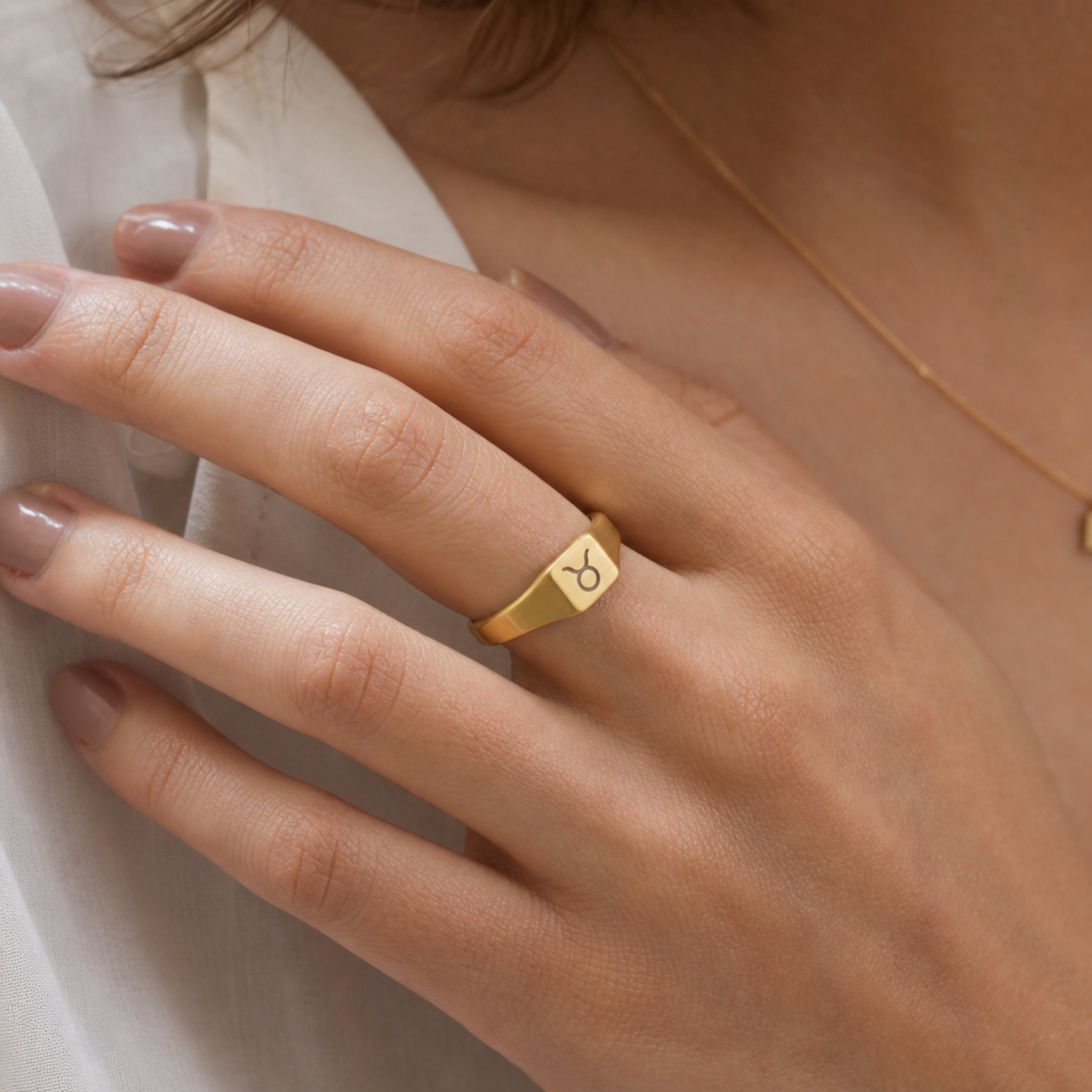 Taurus zodiac square signet ring on finger — model wearing engraved Taurus signet, cream linen lifestyle moment