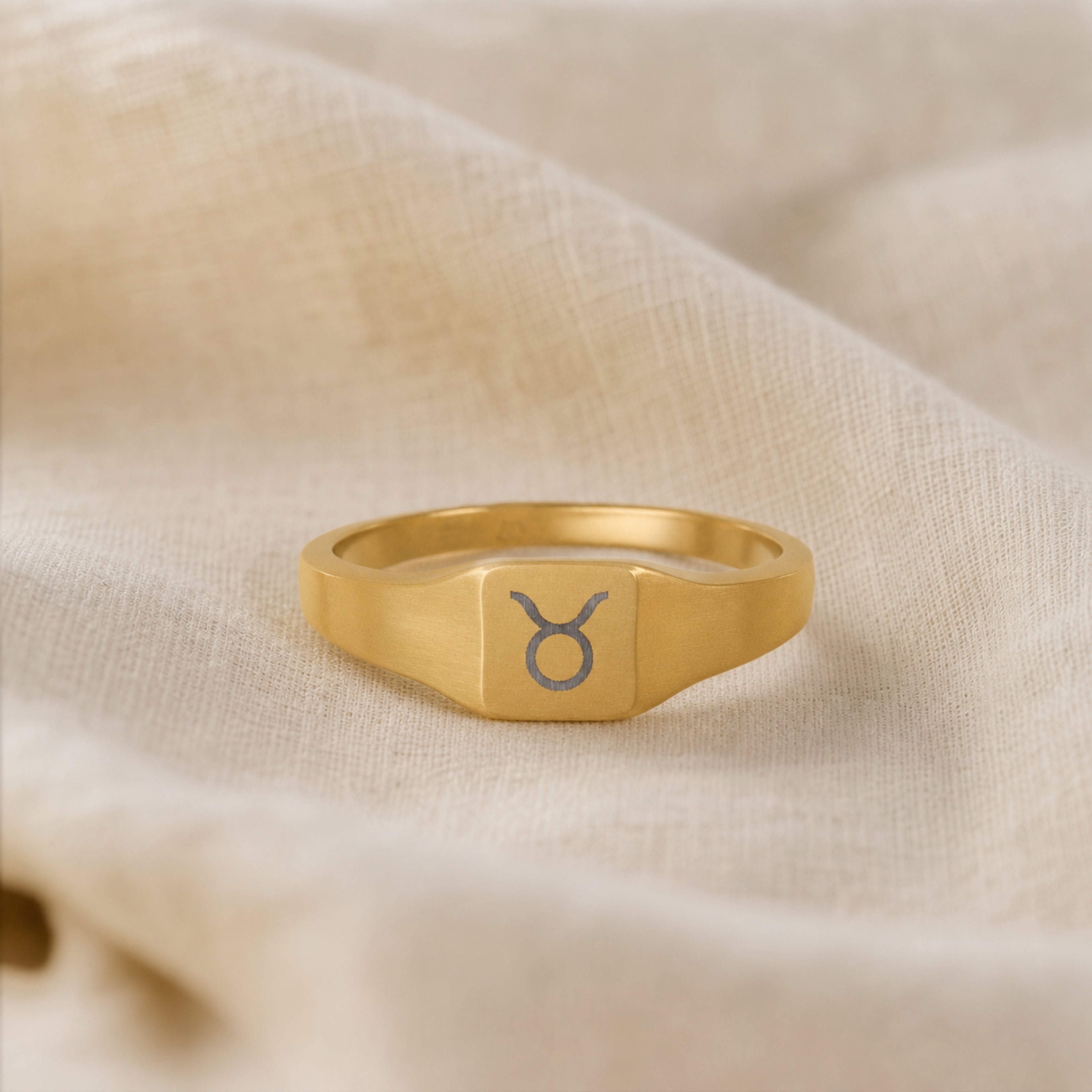 Taurus zodiac square signet ring linen flatlay — engraved Bull ring on rumpled cream linen, editorial product shot