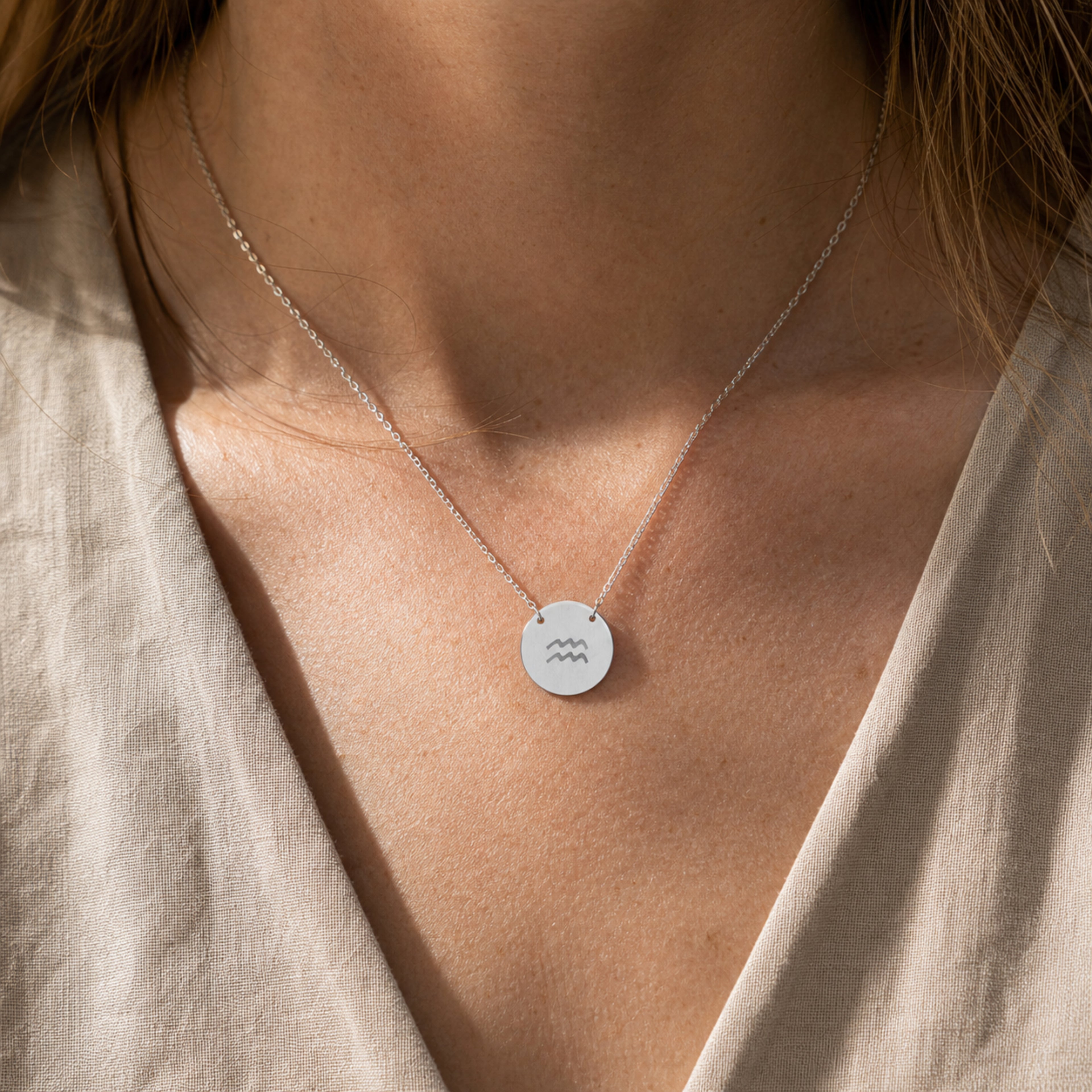 Aquarius zodiac coin necklace worn on model in stainless steel - engraved star sign pendant on neckline (AI-generated image)