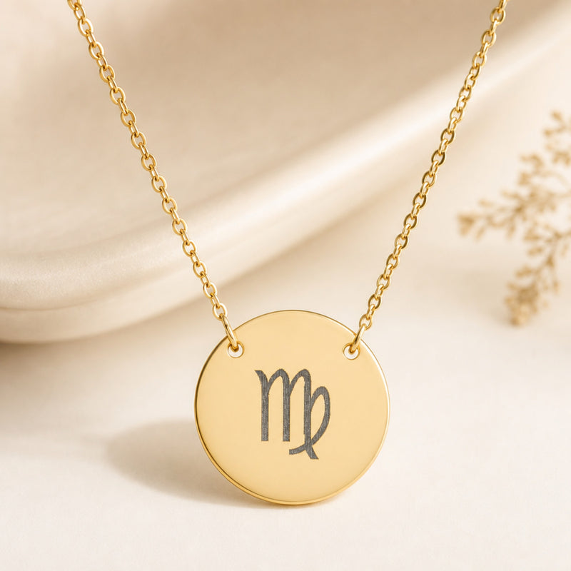 Virgo zodiac sign engraved on a round 18K gold coin pendant necklace, flat lay on cream linen