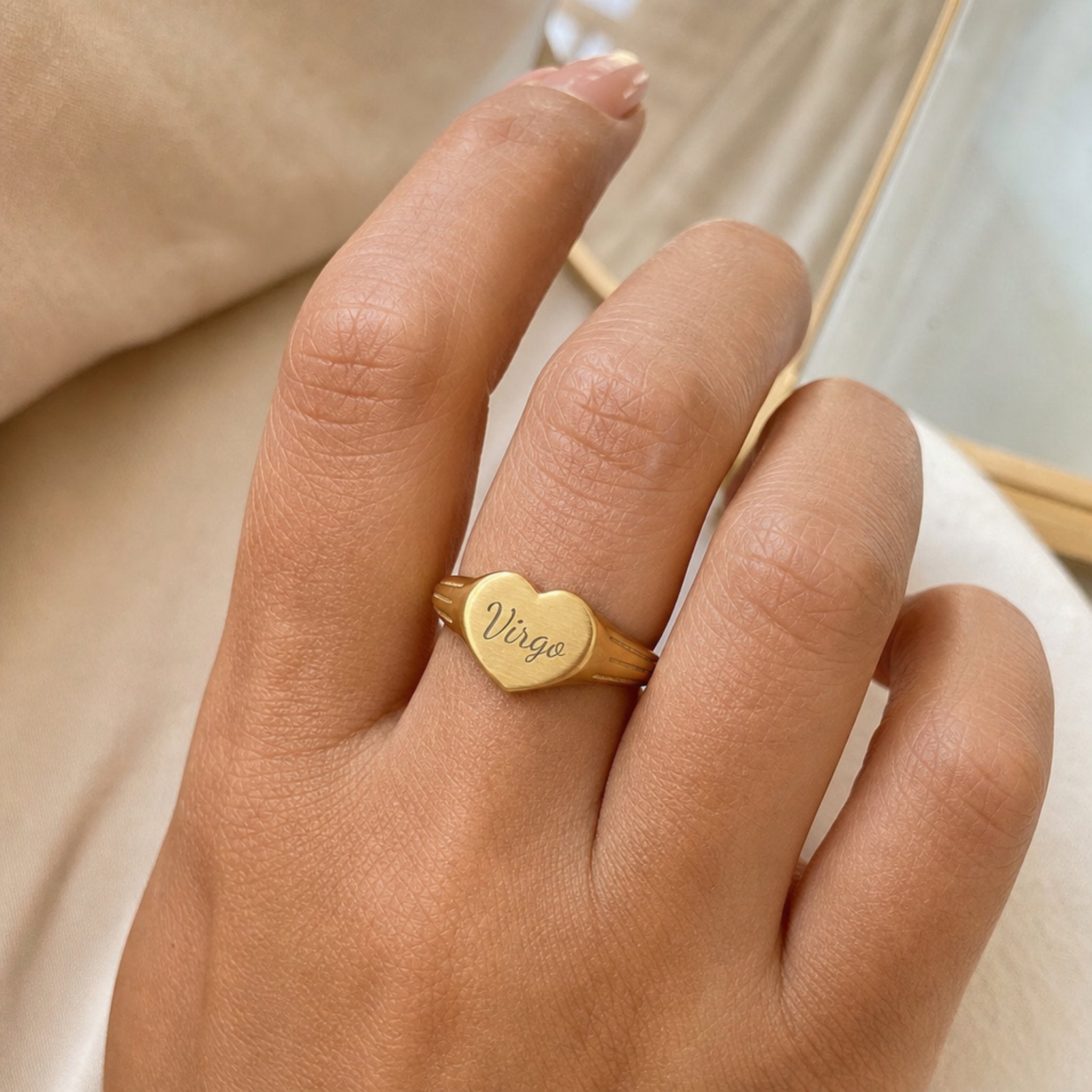 Virgo zodiac heart signet ring on finger — model wearing engraved Virgo heart signet, cream linen lifestyle moment