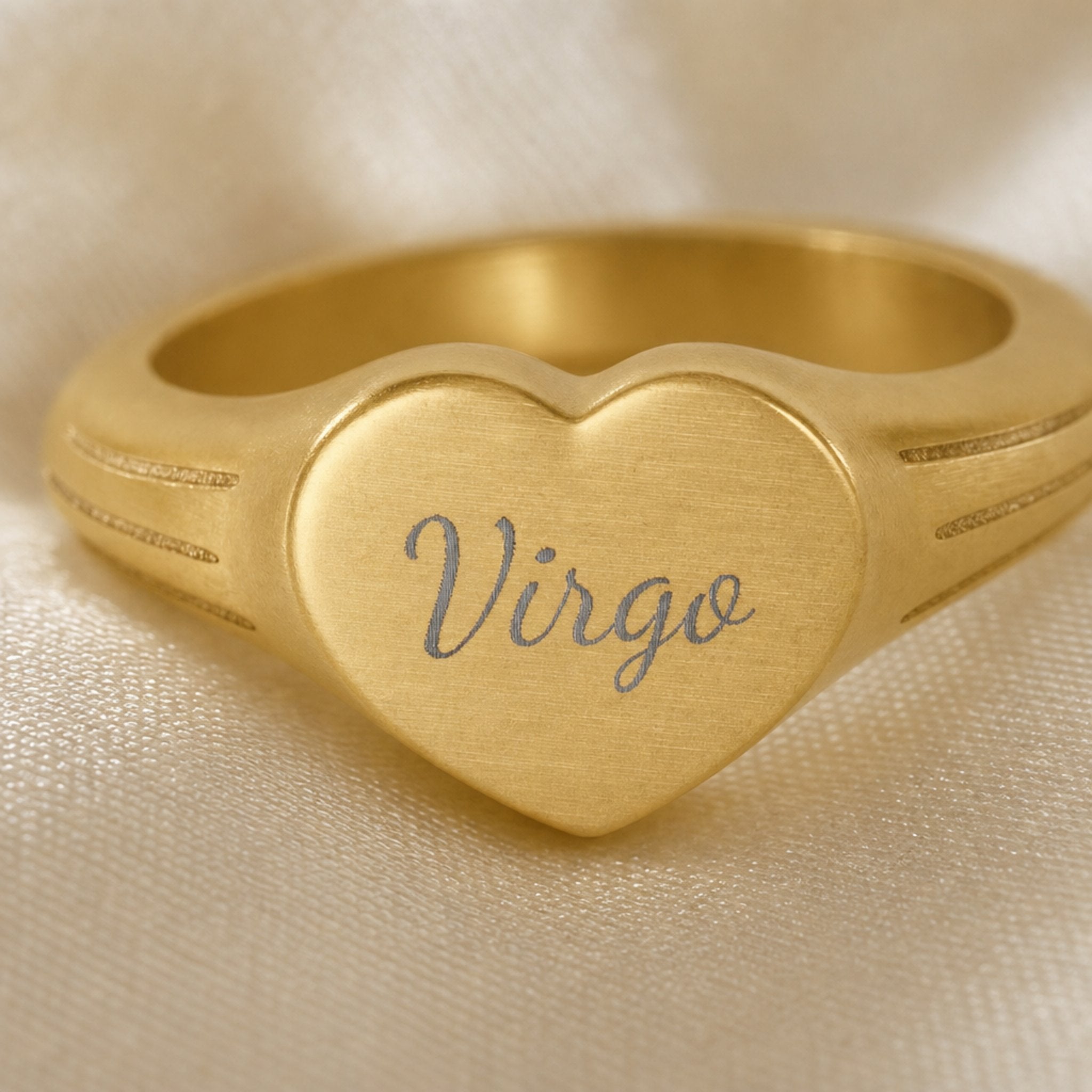 Virgo zodiac heart signet ring engraving close-up — laser-etched Virgo name detail, brushed grey cursive on matte gold heart