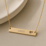 Gold Aries zodiac bar necklace with a slim horizontal bar, laser-engraved with Aries beside an open heart cutout. Memory That Lasts.