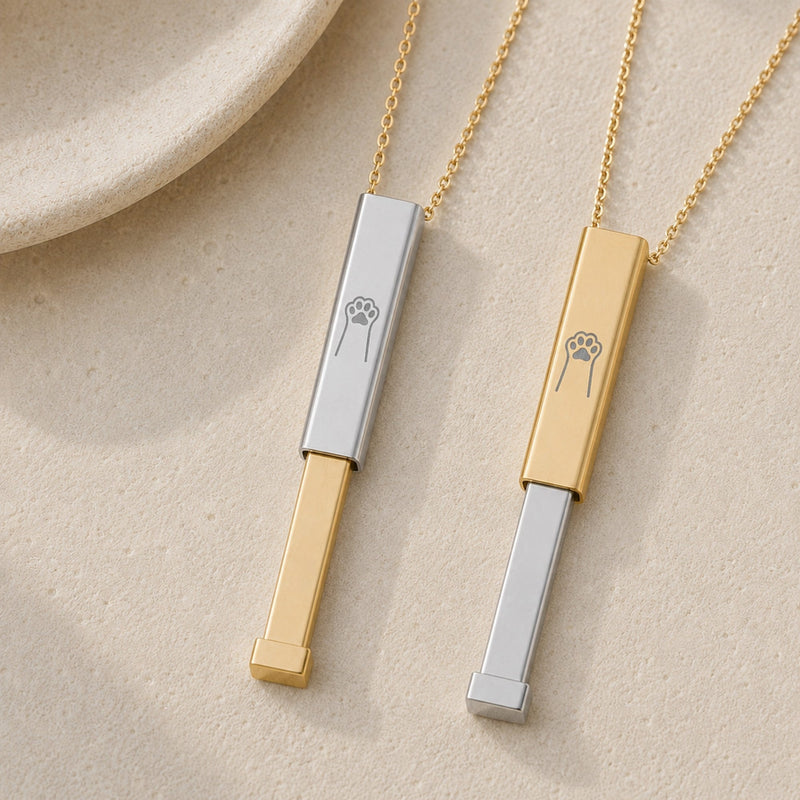 Personalized pet paw print hidden-message sliding bar necklaces in 18K gold and stainless steel, flat lay on cream linen