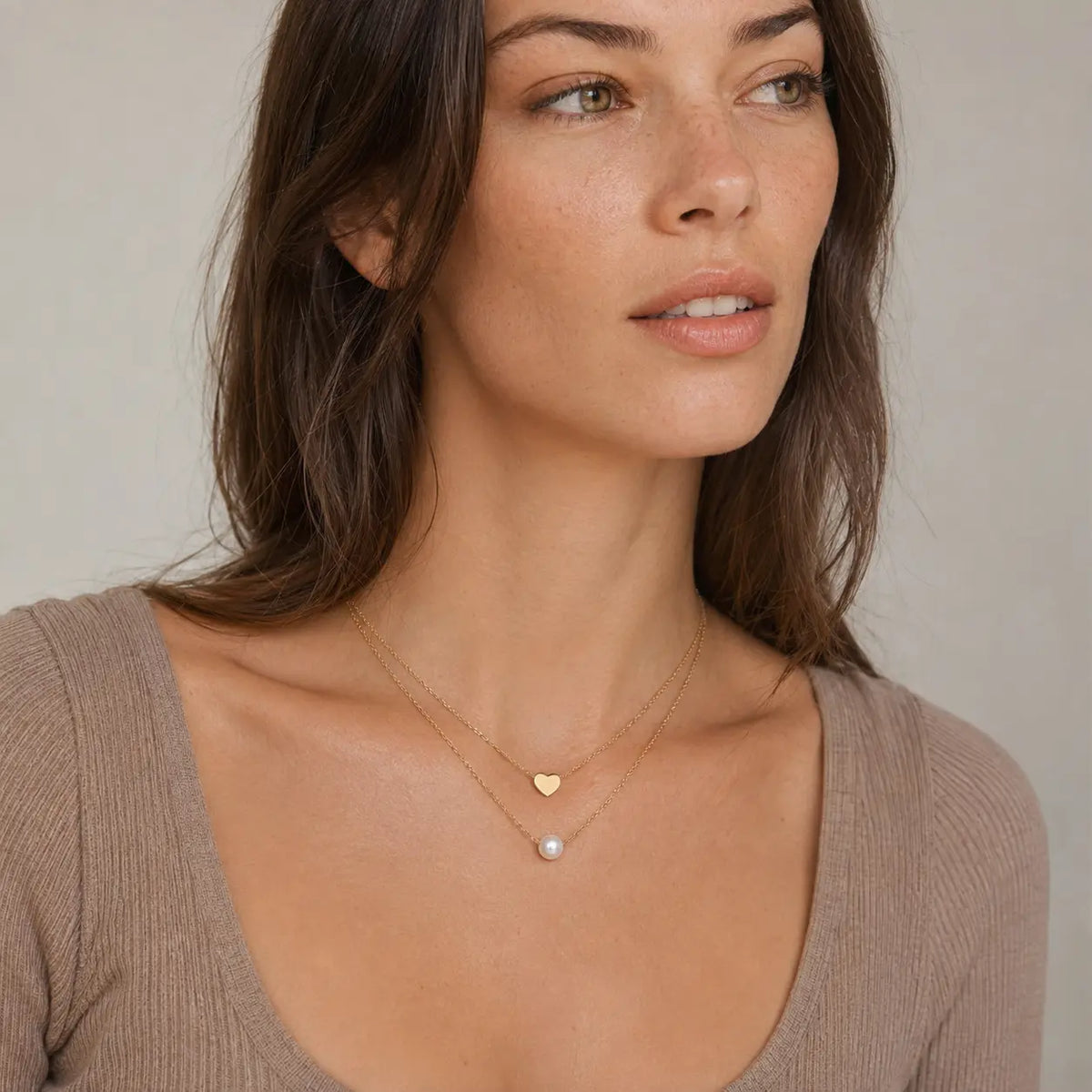 Woman wearing Heart and Pearl Layers gold necklace with a small heart charm and white pearl