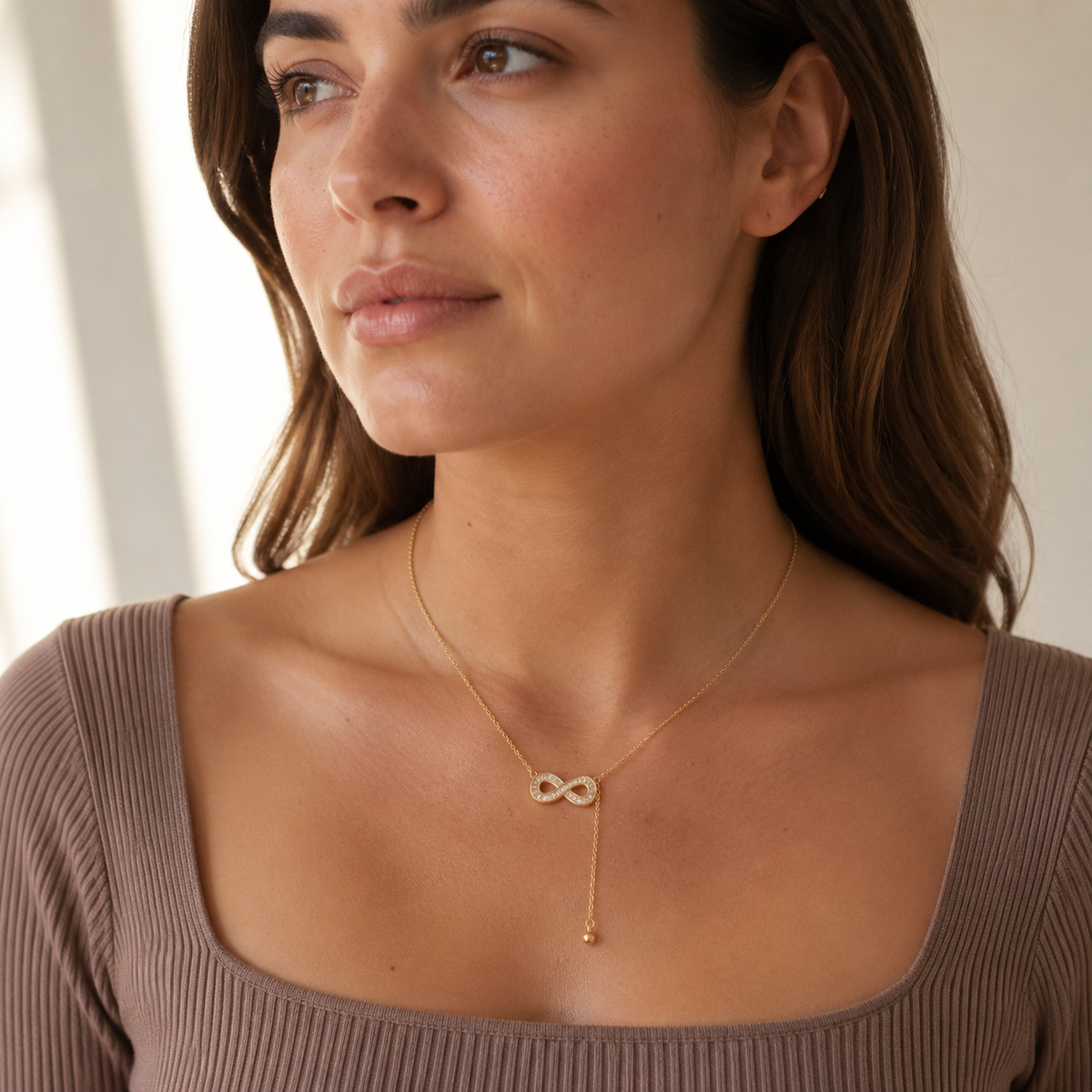 Woman wearing the Infinity Sparkle gold lariat necklace with a collarless taupe knit top