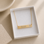 Gold personalized horizontal bar necklace engraved with a custom name beside a cutout heart. Memory That Lasts.